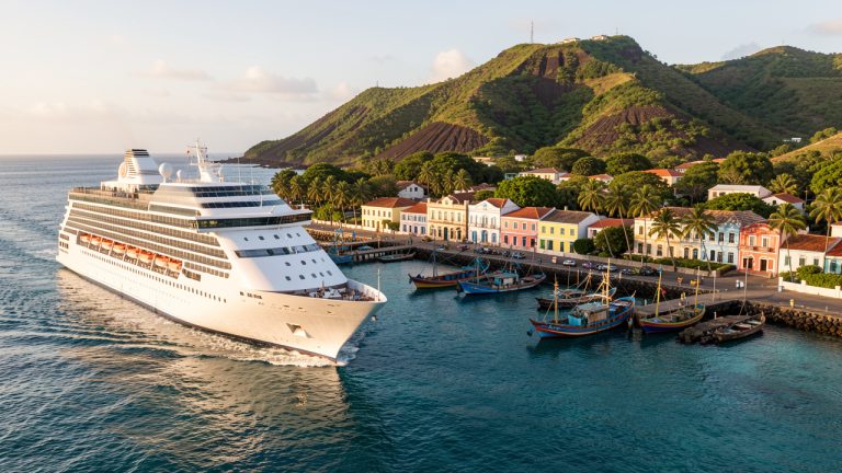 Navire de croisière approchant une véritable escale caribéenne aux maisons colorées, entourée de palmiers, de bateaux de pêche et de collines volcaniques.